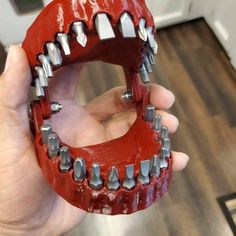 a person holding up a fake red tooth with metal spikes on it's teeth