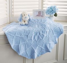 a baby blanket on a window sill next to a teddy bear and flower vase