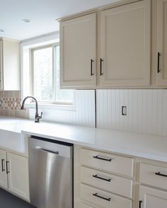 a clean kitchen with white cabinets and stainless steel dishwasher, sink and window