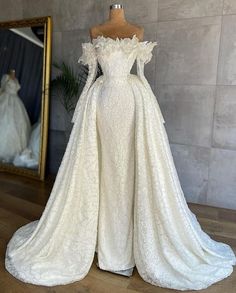 a white wedding gown on display in front of a mirror with a dress hanging from it's back