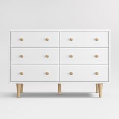 a white dresser with wooden legs and knobs on the top, in front of a white wall