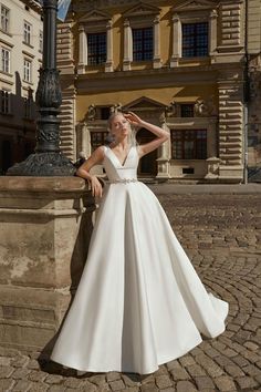 a woman in a white wedding dress leaning against a stone wall and posing for the camera