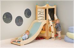 two toddlers playing in a play room with a slide and climbing wall behind them