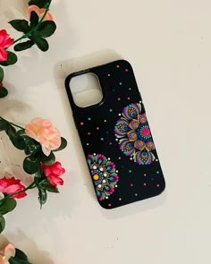 a black phone case with colorful flowers and polka dots on the back is laying next to some pink roses