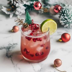 a drink with lime and pomegranate garnish in a glass surrounded by christmas decorations