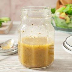 a glass jar filled with liquid sitting on top of a table next to a salad