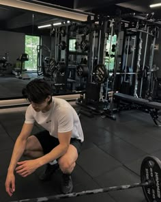 a man squatting down in front of a barbell rack with one hand on the ground