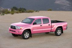 a pink pick up truck parked in a parking lot with mountains in the back ground