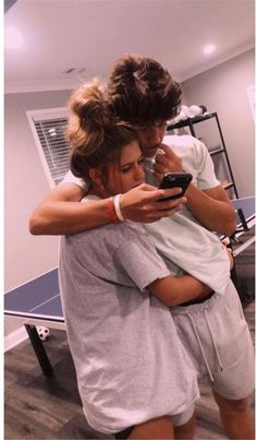 two people hugging each other while looking at a cell phone