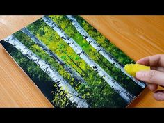 a person is holding a piece of yellow paper in front of a painting on a wooden table