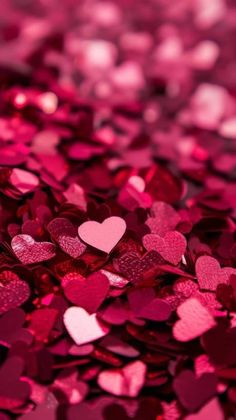 many pink hearts are scattered together on the ground in this close up photo, which is very bright and shiny