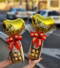 two heart shaped chocolates wrapped in foil and tied with red ribbon are held by someone's hand