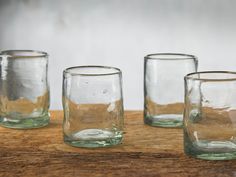 four glasses sitting on top of a wooden table next to each other with water in them