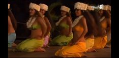 several women in yellow skirts and headdresses sitting on the ground with their hands behind their backs