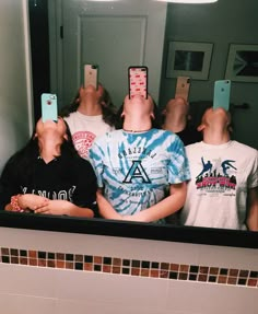 three people taking selfies in the bathroom mirror with their cell phones up to their heads