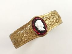 "This is an interesting piece - I have looked at it for a long time and spent (too much :) time trying to identify the signature. I was ultimately unsuccessful, which means it's a pretty obscure manufacturer*. This is a gold finished bracelet featuring a clear red glass oval on top of which was set a black oval stone on top of which is a white cameo. I'm going to go with the idea that this is (like so many other bracelets constructed like this one) a 30s bracelet - but there is the chance that t Victorian Adjustable Bangle - Gift, Victorian Adjustable Bangle As A Gift, Victorian Style Bangle As A Gift, Red Adjustable Cuff Bracelet For Wedding, Adjustable Red Cuff Bracelet For Wedding, Vintage Red Bracelets For Wedding, Vintage Red Bracelet For Wedding, Vintage Red Bracelet As A Gift, Vintage Red Bracelet For Gifts