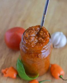 a jar filled with sauce sitting on top of a wooden table next to some vegetables