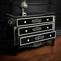 a black and white chest of drawers sitting on top of a wooden floor next to a vase