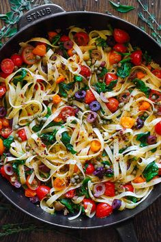 a pan filled with pasta and vegetables on top of a wooden table