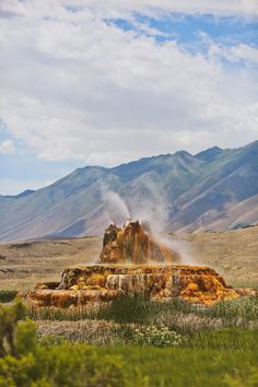 an old geyser spewing out water into the air with mountains in the background