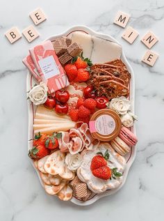 a platter filled with cheese, strawberries and other food items next to scrabble letters