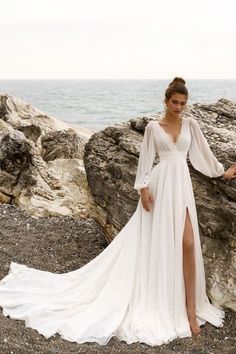 a woman in a long white dress standing on rocks near the ocean with her legs spread out