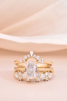 two gold wedding rings with an oval shaped diamond on top and round brilliant cut diamonds on the bottom