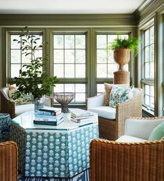 a living room with wicker furniture and large windows in the corner, along with books on a coffee table