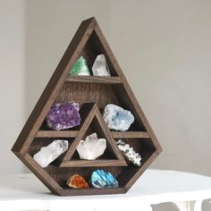 a wooden shelf filled with different types of rocks on top of a white table next to a wall