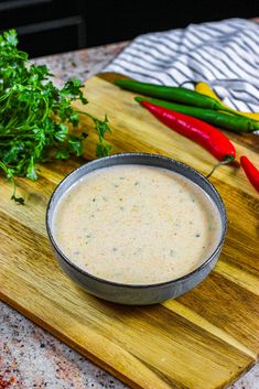 a wooden cutting board topped with a bowl of dip next to peppers and parsley