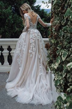 a woman in a wedding dress standing next to a tree and looking down at the ground