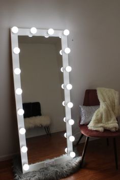 a lighted mirror sitting on top of a hard wood floor next to a red chair