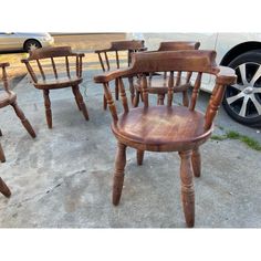 four wooden chairs sitting on concrete next to a car