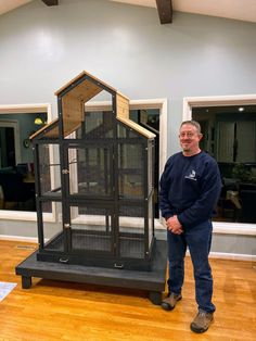 a man standing next to a large bird cage in a room with wooden floors and walls