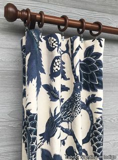 a close up of a blue and white curtain with birds on it hanging from a wooden rod