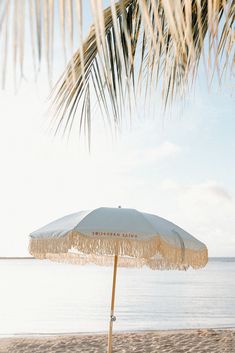 an umbrella sitting on top of a sandy beach next to the ocean and palm trees