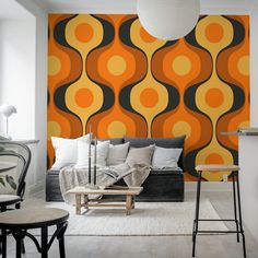 a living room with an orange and black pattern on the wall next to two stools