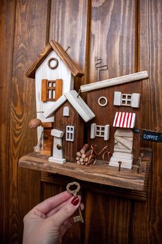 a hand holding a key to a small wooden house on a shelf with other items