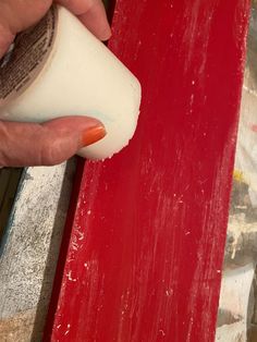 a person is painting a piece of wood with red and white paint on the top