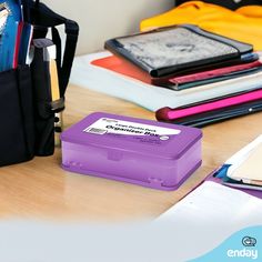 a purple lunch box sitting on top of a wooden table next to notebooks and folders