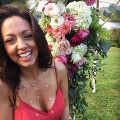 a beautiful woman in a red dress standing next to a flower covered pole with pink and white flowers on it