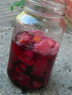 a glass jar filled with liquid sitting on top of a cement ground next to a brick wall