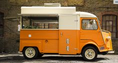 an orange and white food truck parked in front of a brick building