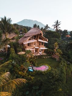 an aerial view of a tropical house surrounded by trees and greenery, with mountains in the background