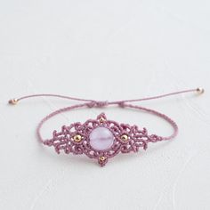 a pink bracelet with gold beads on a white surface, the bead is attached to an adjustable cord