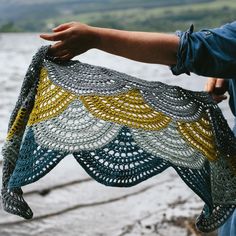 a person holding up a crocheted shawl by the water