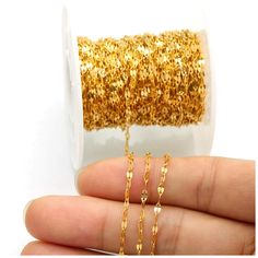 a hand holding a spool of gold glitter on a roll of tape with a chain attached to it