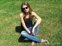 a woman sitting on the grass with her hands in her pockets and looking at the camera