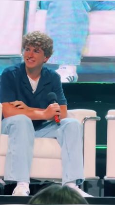 a man sitting on top of a white chair in front of a crowd at an event