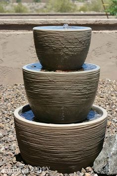 there are three bowls on top of each other in the sand and gravel, with water running down them